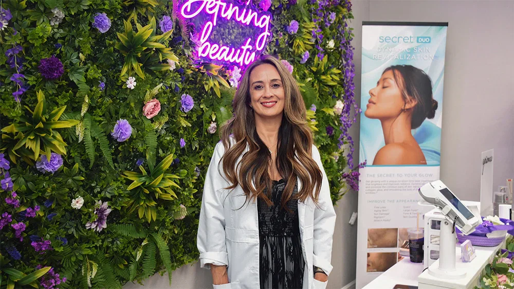 Professional Medical worker standing in modern beauty salon with purple floral wall and neon sign - in Tampa, FL
