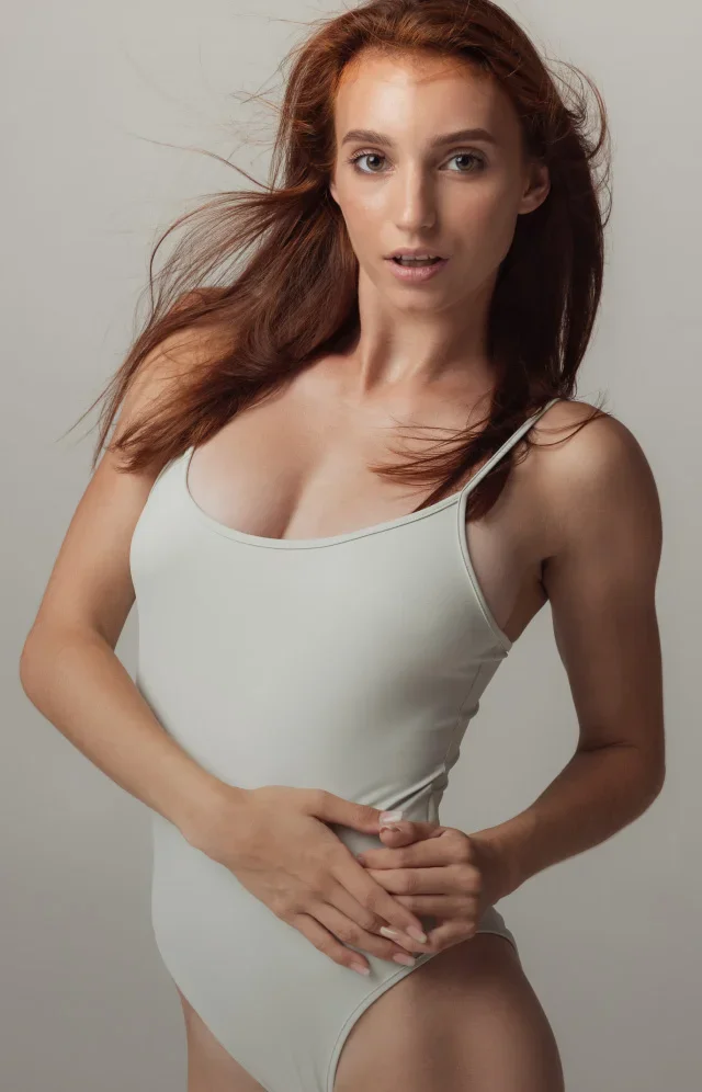 Woman in white bodysuit with long red hair posing against neutral background - RF microneedling in Tampa, FL