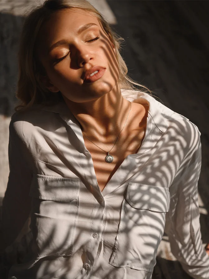 Woman with closed eyes in striped shirt enjoying warm sunlight creating shadow patterns on her face - Acne conditions in Tampa, FL