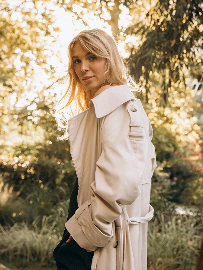 Blonde woman in cream off-shoulder jacket standing outdoors in golden sunlight among trees - chemical peels in Tampa, FL