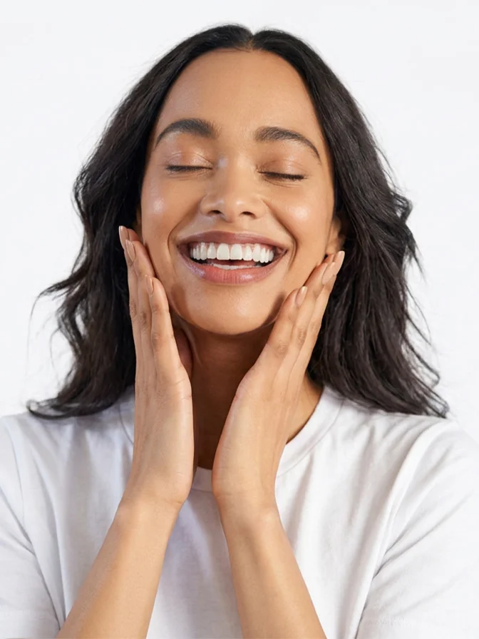 Woman with glowing skin smiling joyfully while touching her face, wearing white shirt on light background - Hollywood spectra in Tampa, FL