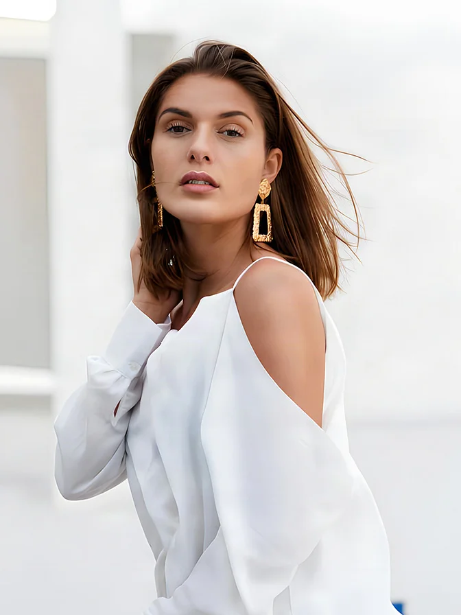 Woman wearing white cold shoulder top with statement earrings looking over shoulder in natural light - Smoothlase in Tampa, FL